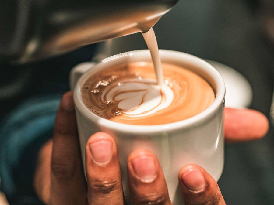 Una mano sosteniendo una taza con un diseño de arte latte.