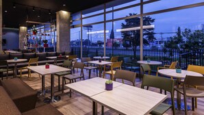 A modern restaurant with large windows, seating arrangements, and a view of the cityscape. - ibis Chia (Chia)