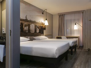 A hotel room with two beds, a desk, a wall mural, and a window with curtains. - ibis Chia (Chia)