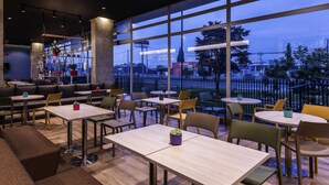A modern restaurant with large windows, seating arrangements, and a view of the cityscape. - ibis Chia (Chia)
