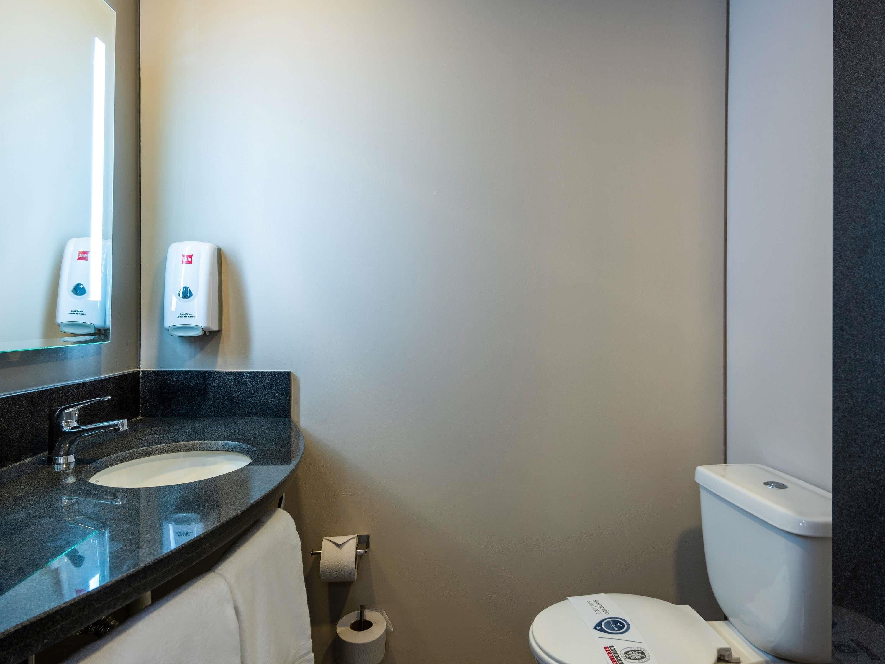 A bathroom with a sink, mirror, toilet, and hand sanitizer dispensers.