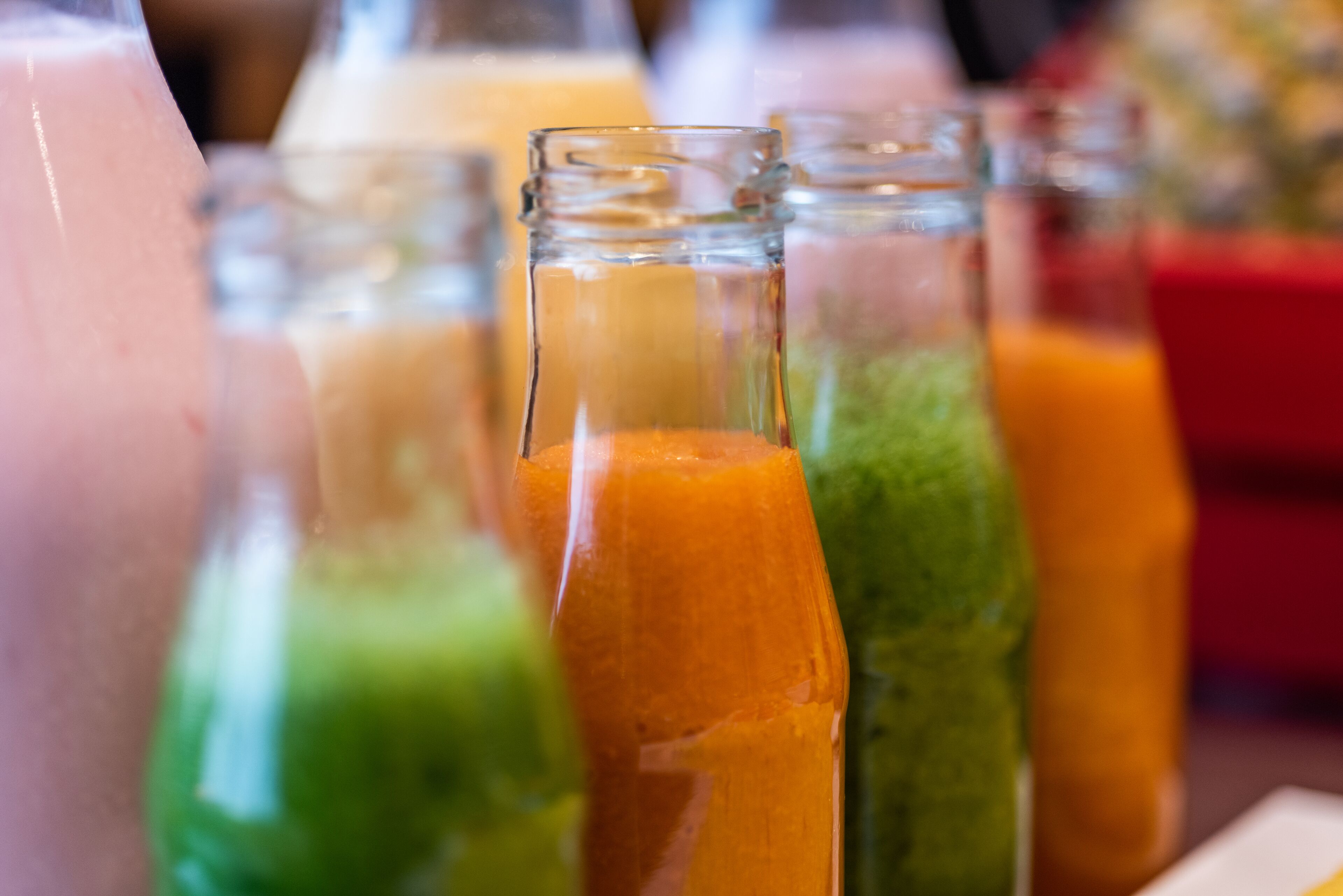 Een rij glazen flessen met verschillende soorten vloeistoffen, waarschijnlijk vruchtensappen of smoothies.