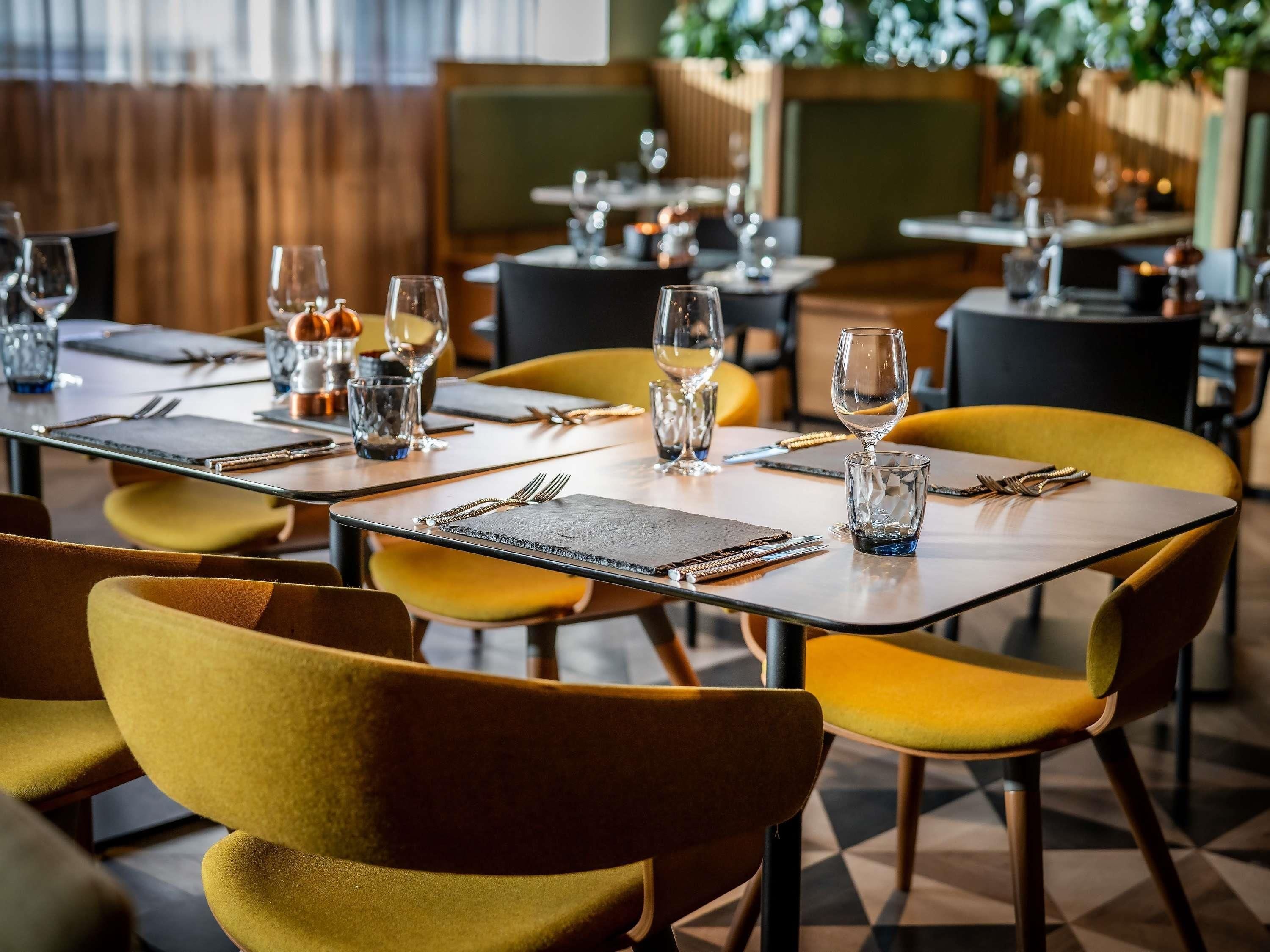 A restaurant with tables set for dining, featuring yellow chairs and a geometric floor pattern.