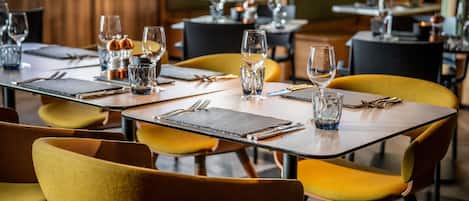 A restaurant with tables set for dining, featuring yellow chairs and a geometric floor pattern.