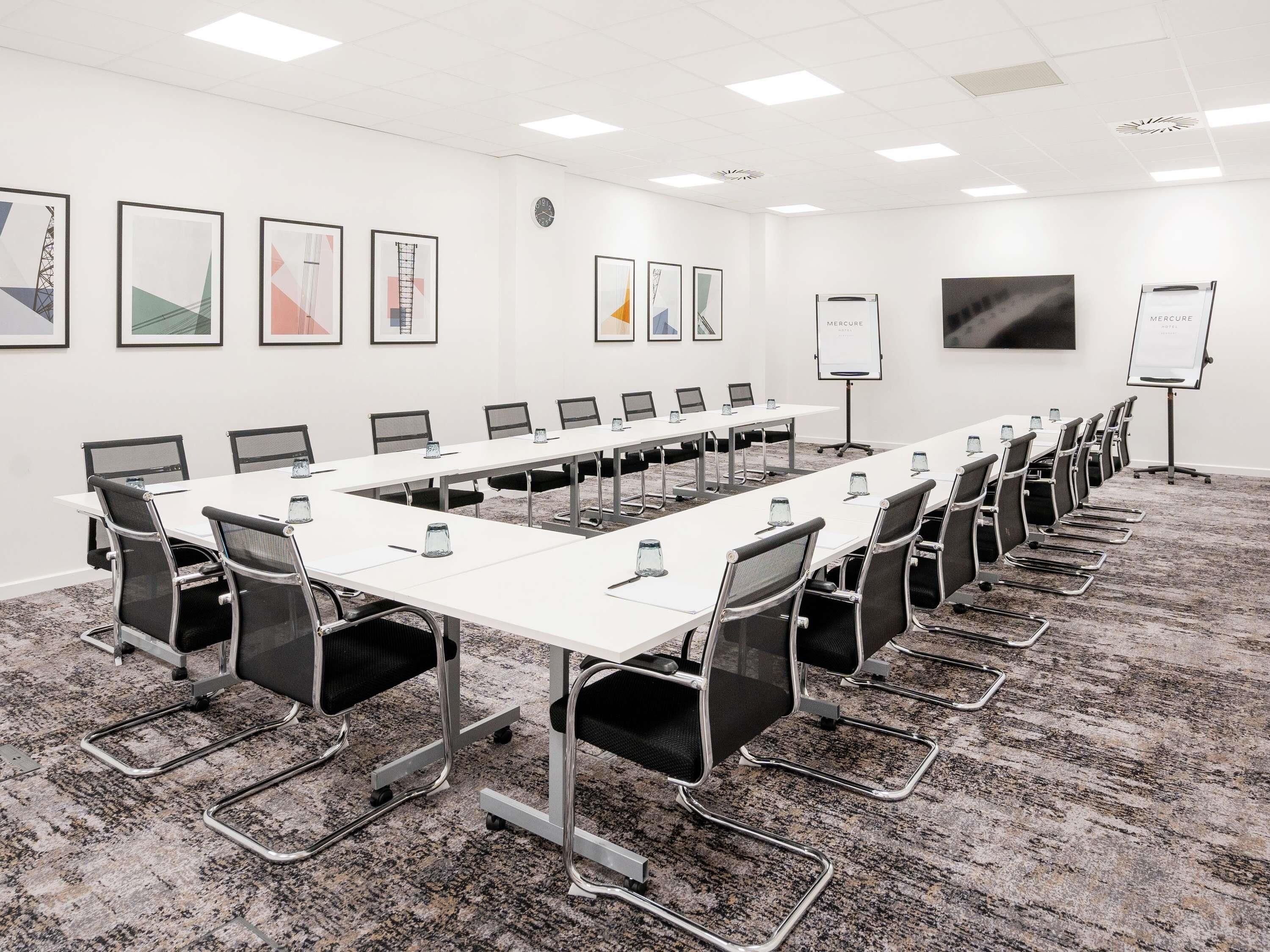 Un salón de conferencias con una larga mesa, sillas, computadoras portátiles y una pizarra.