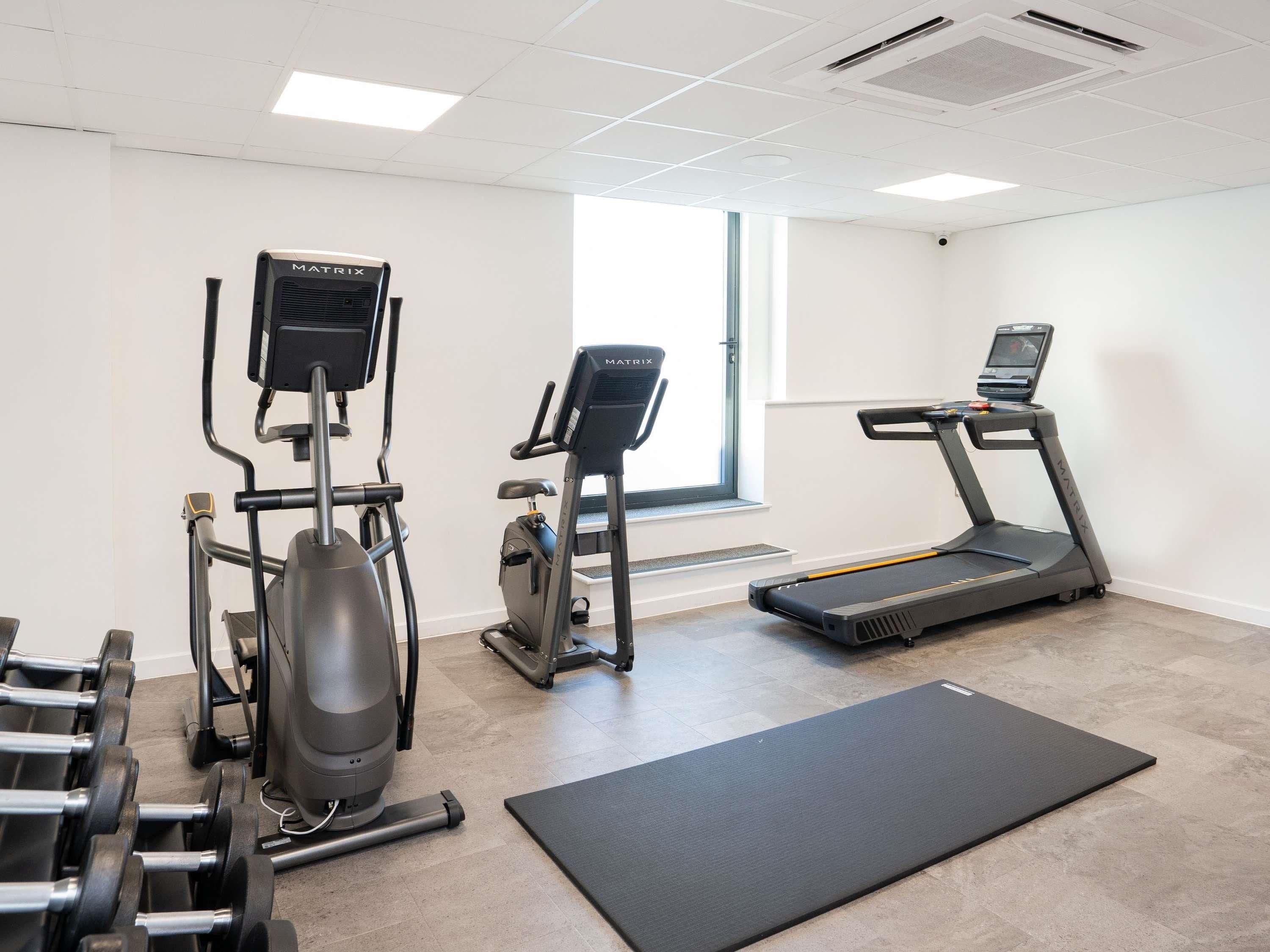 Una palestra con macchinari cardio, pesi e un tappetino da yoga.