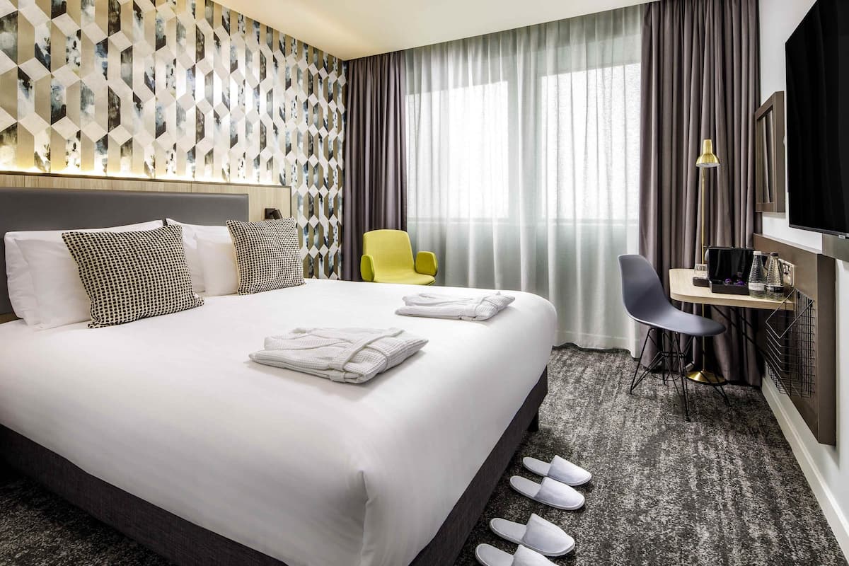 A hotel room with a large bed, a desk with a chair, a TV, and a window with curtains.