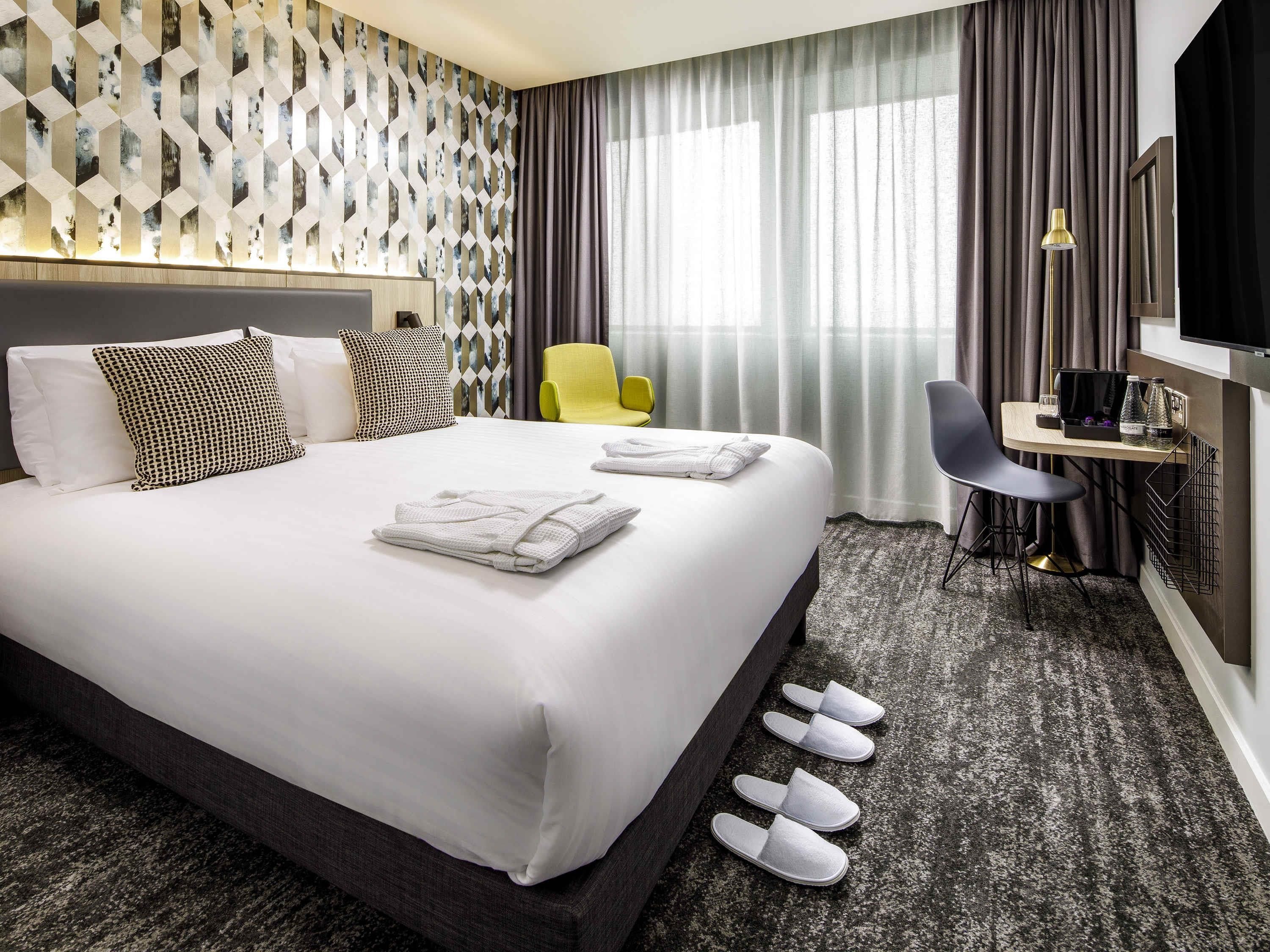 Una habitación de hotel con una cama grande, un escritorio con silla, un televisor y una ventana con cortinas.