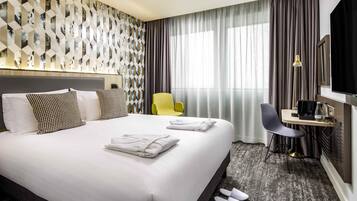 Una habitación de hotel con una cama grande, un escritorio con silla, un televisor y una ventana con cortinas.