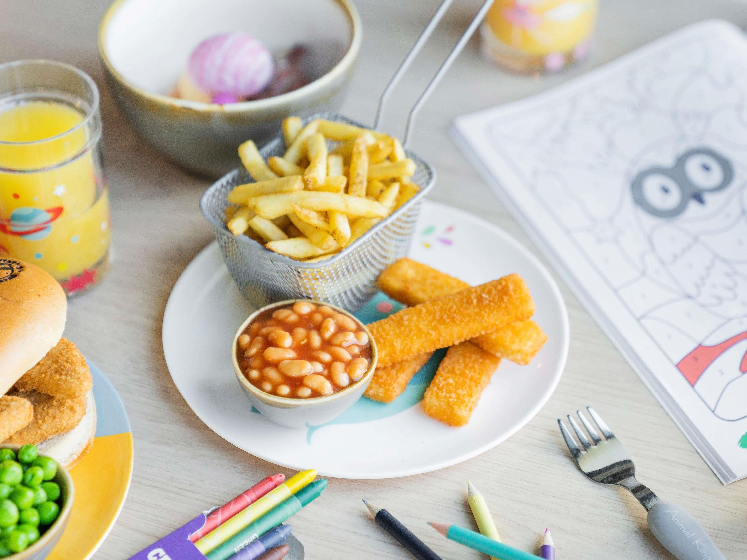 A plate with French fries, baked beans, and breaded fish fingers.