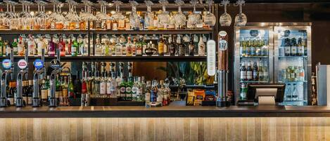Uma área de bar com várias torneiras, prateleiras cheias de garrafas e um espaço para sentar com cadeiras.