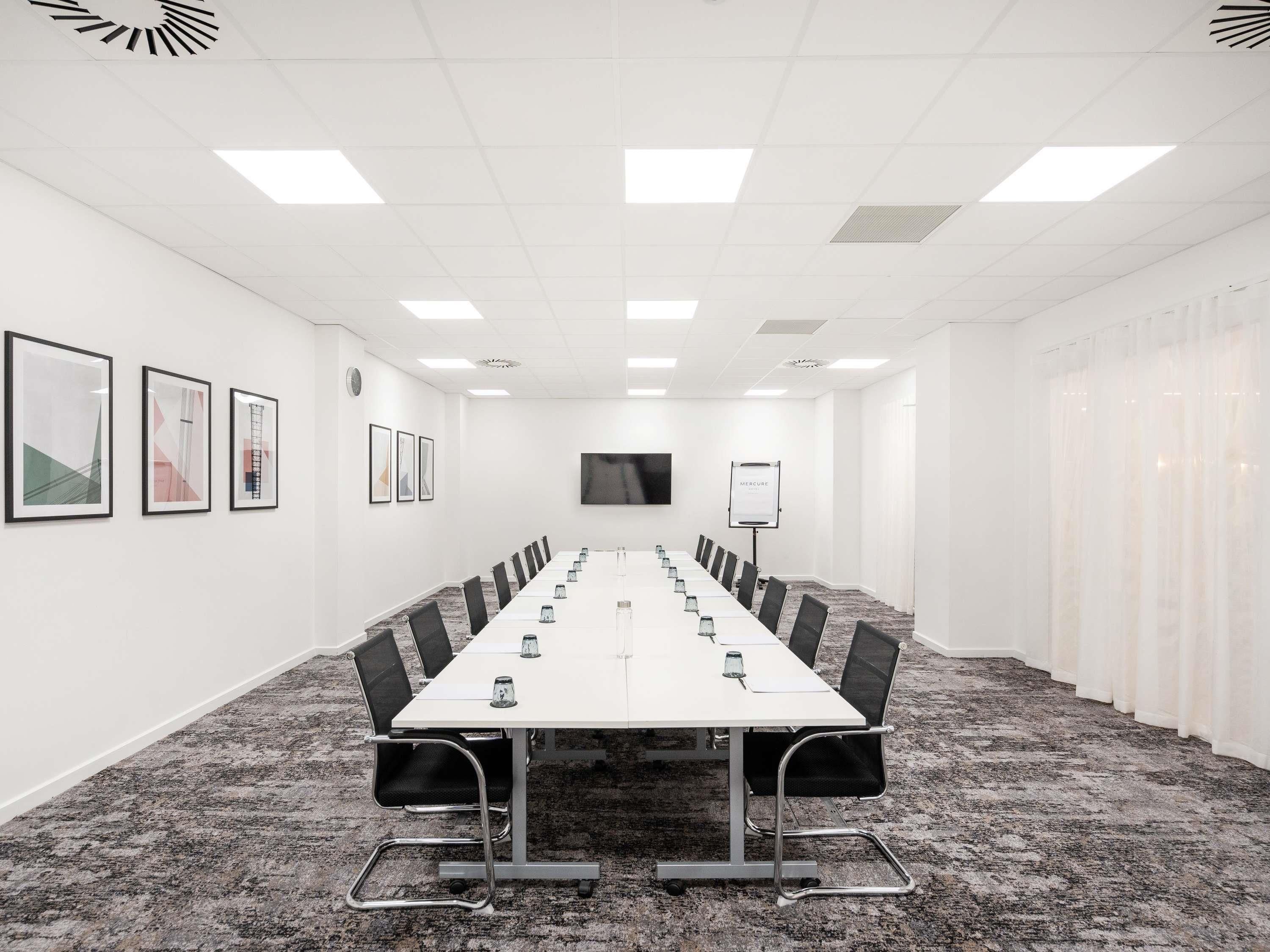 A conference room with a long table, chairs, a projector screen, and a whiteboard.