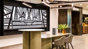 A reception area with a modern design, featuring a reception desk, two chairs, a potted plant, and a decorative wall panel. - Mercure Newport Hotel (Newport)