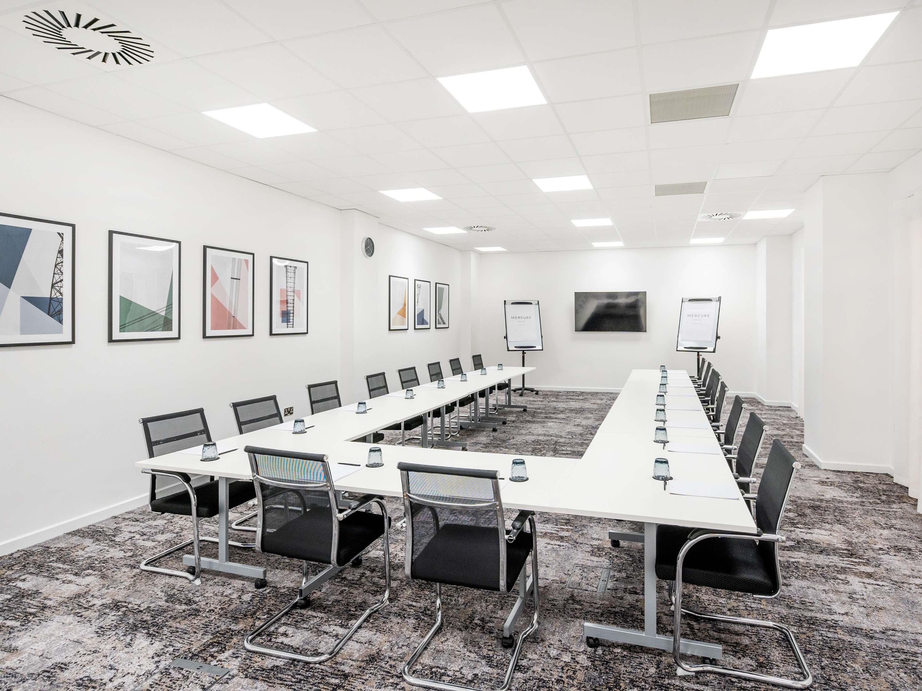 A conference room with a long table, chairs, a clock, framed artwork, and a whiteboard.