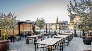 An outdoor patio with tables and chairs, potted plants, and a view of buildings in the background. - Mercure Newport Hotel (Newport)