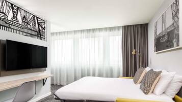 A hotel room with a bed, a desk, a TV, a chair, and a small table.