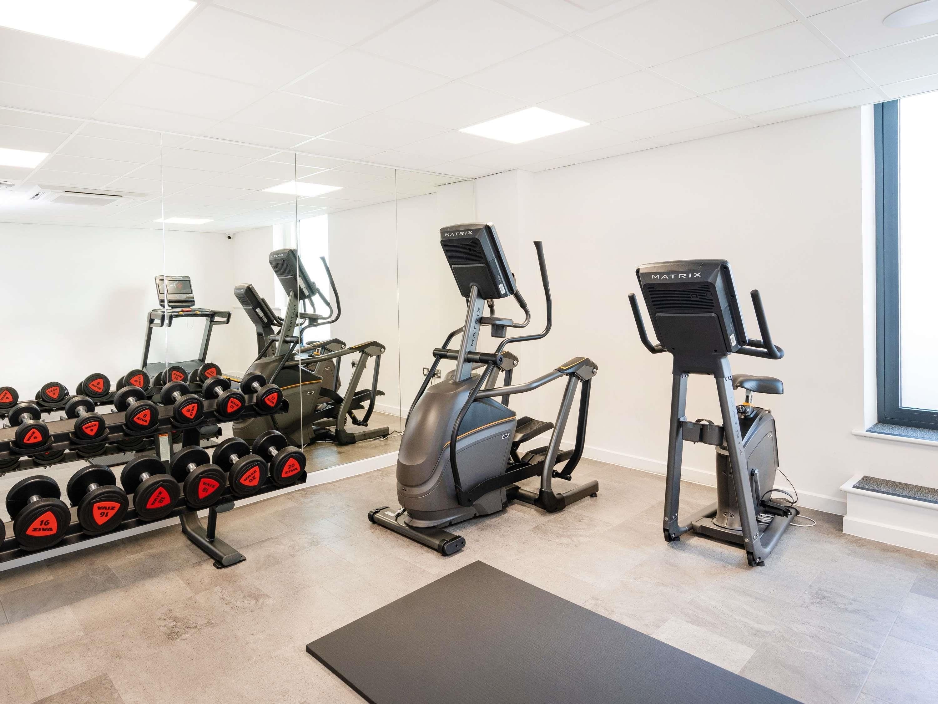 Ein Fitnessstudio mit Laufbändern, Crosstrainern und einer Hantelbank.