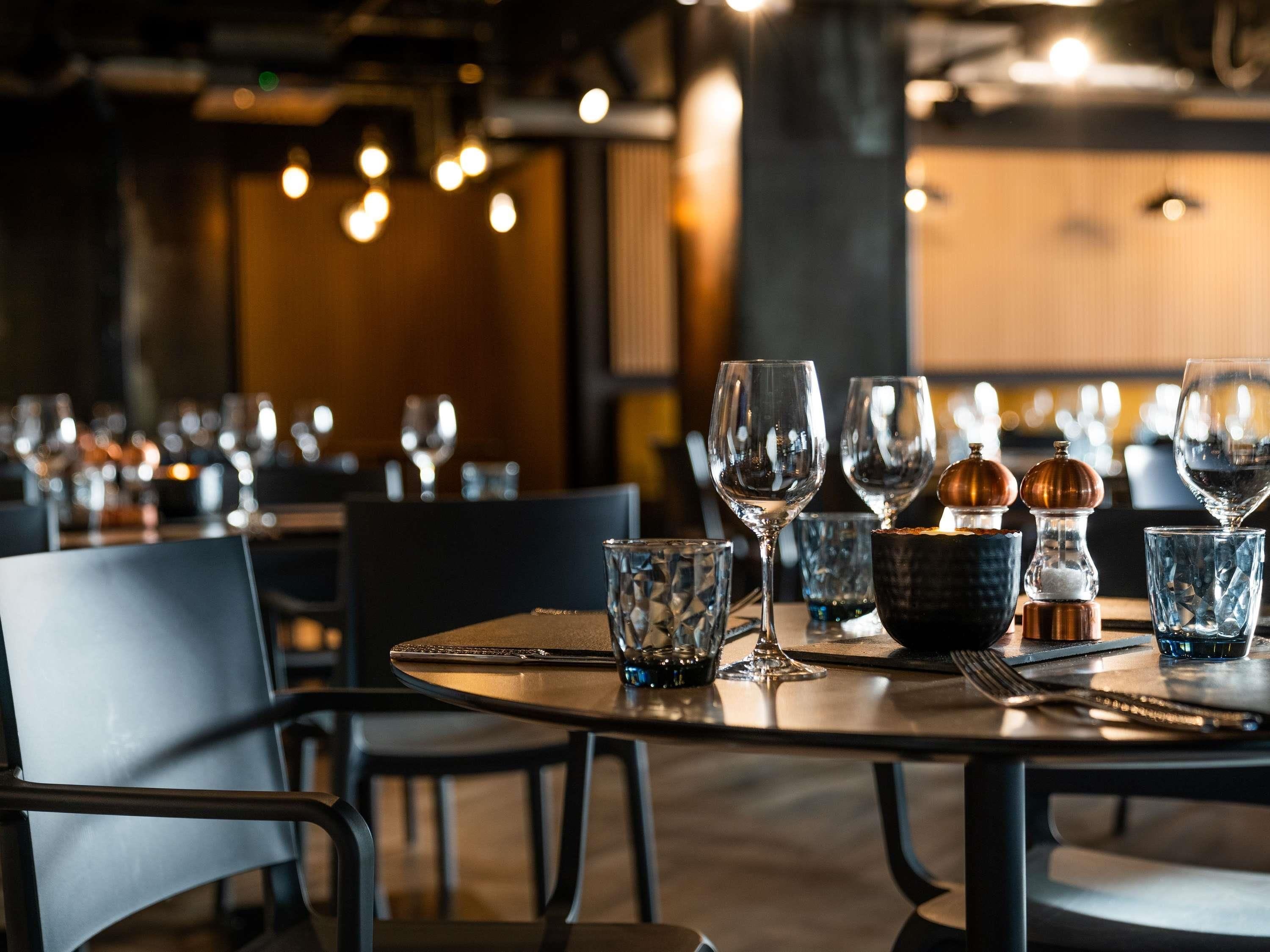Un restaurant où les tables rondes sont dressées avec des verres à vin, des couverts et des salières et poivrières.