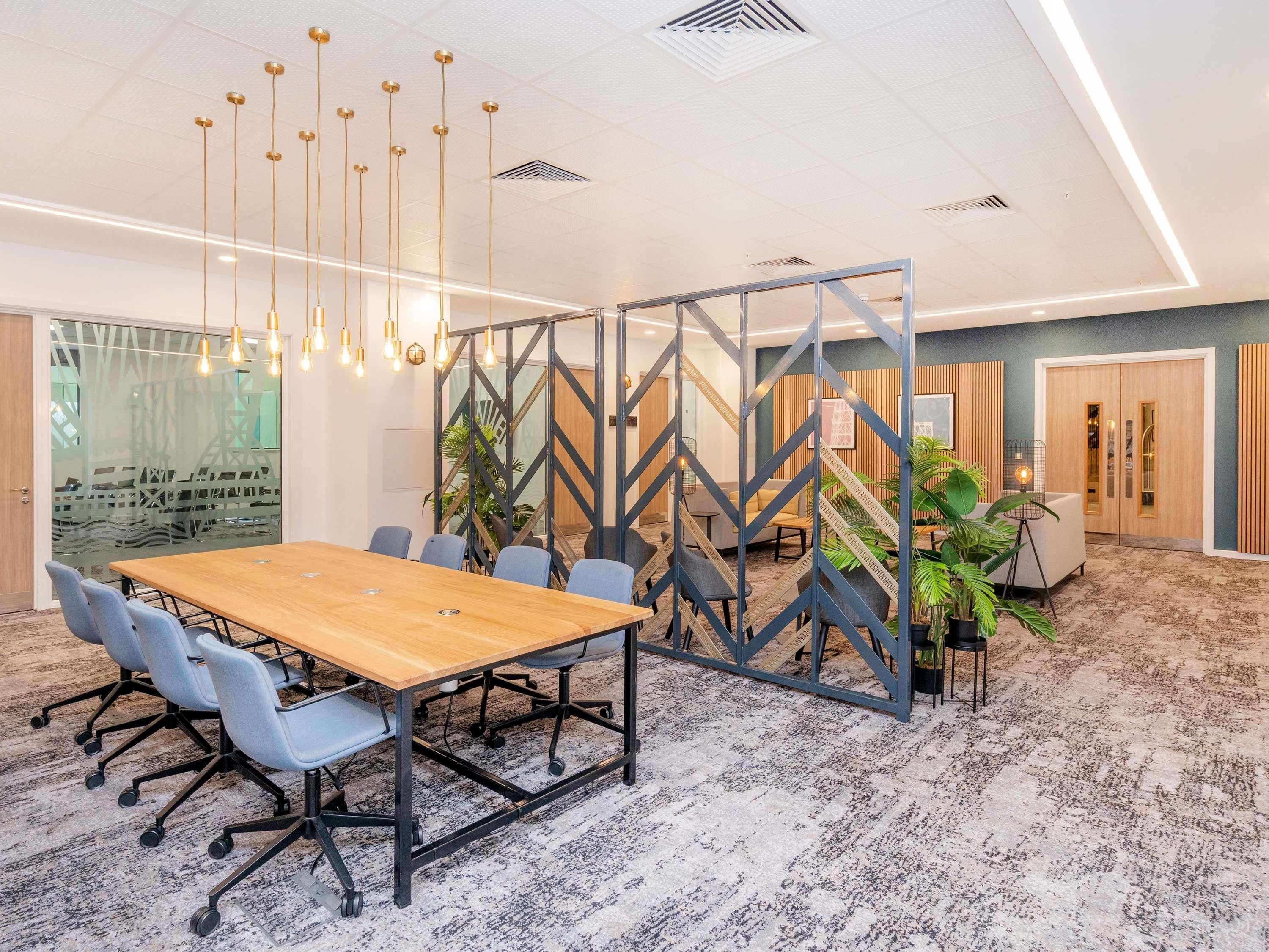 A conference room with a large wooden table, blue chairs, and hanging pendant lights.