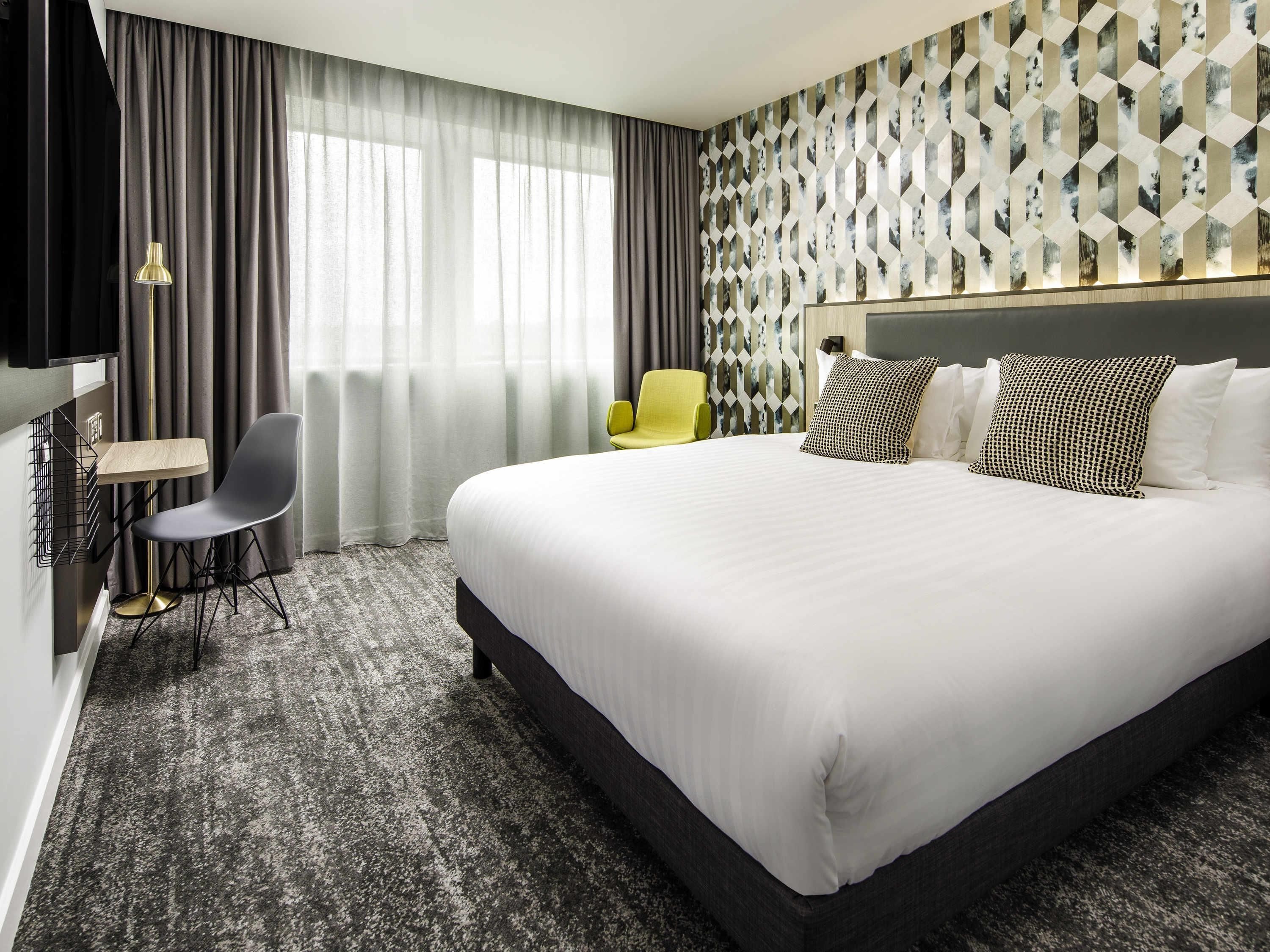 Ein Hotelzimmer mit einem großen Bett, einem Schreibtisch mit Stuhl, einem Fernseher und einer Wand mit Muster.