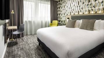 Ein Hotelzimmer mit einem großen Bett, einem Schreibtisch mit Stuhl, einem Fernseher und einer Wand mit Muster.
