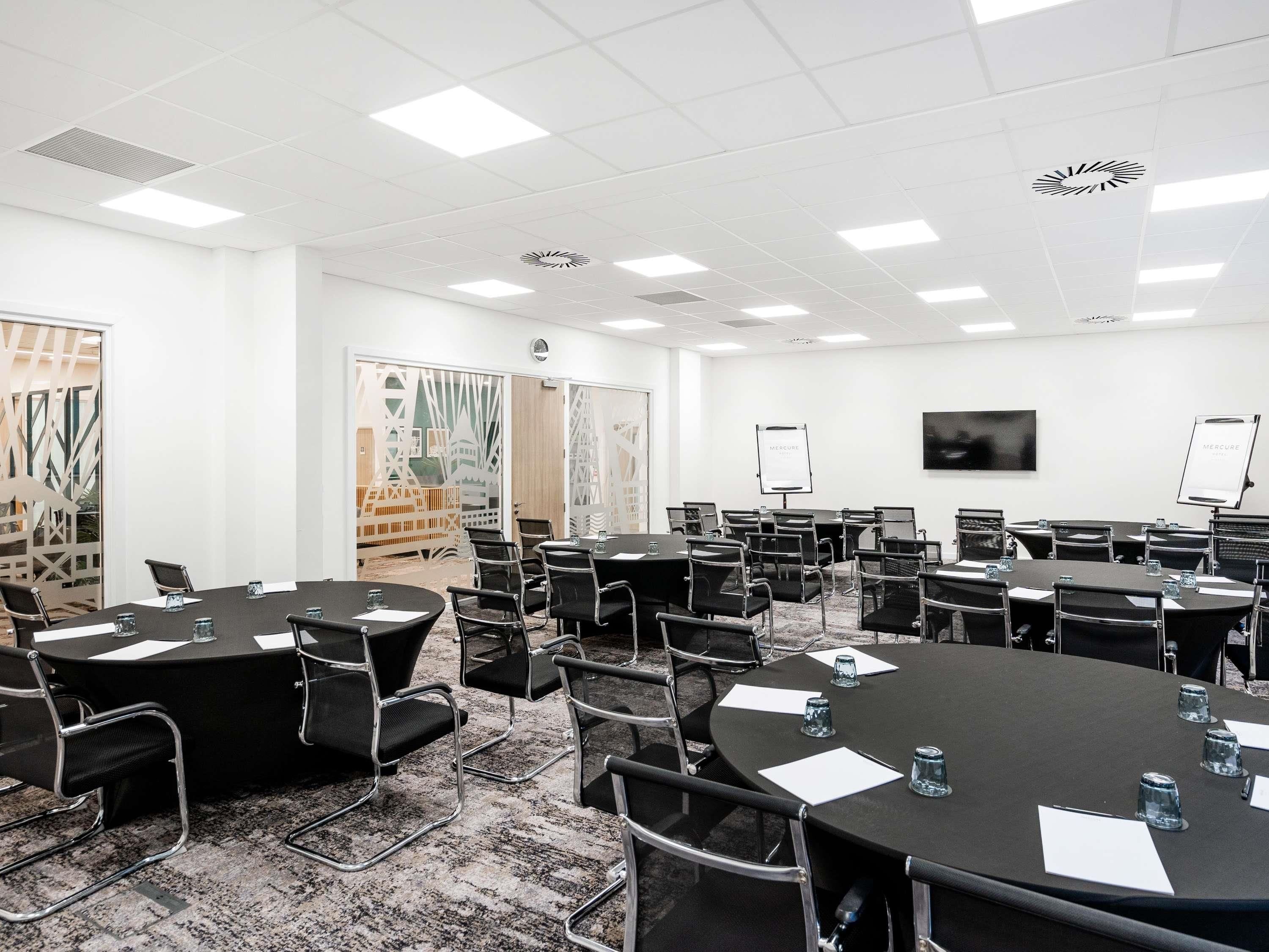 A conference room with multiple tables, chairs, a projector screen, and a whiteboard.