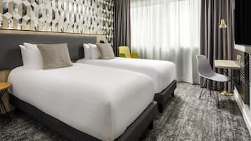Habitación de hotel con dos camas, un escritorio, una silla y un ventanal con cortinas.