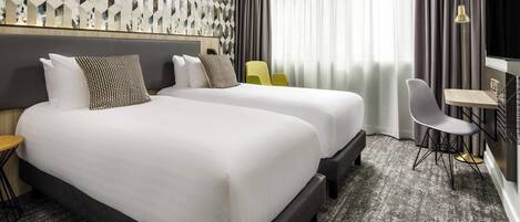 Habitación de hotel con dos camas, un escritorio, una silla y un ventanal con cortinas.