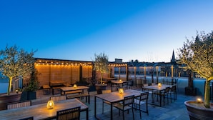 An outdoor patio with wooden tables and chairs, string lights, and potted plants. - Mercure Newport Hotel (Newport)