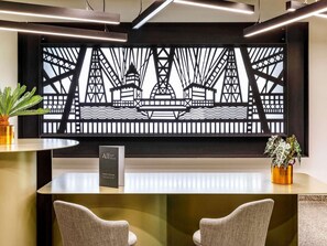 A reception desk with a modern design, featuring a large black and white artwork of a bridge and buildings, two chairs, and potted plants. - Mercure Newport Hotel (Newport)