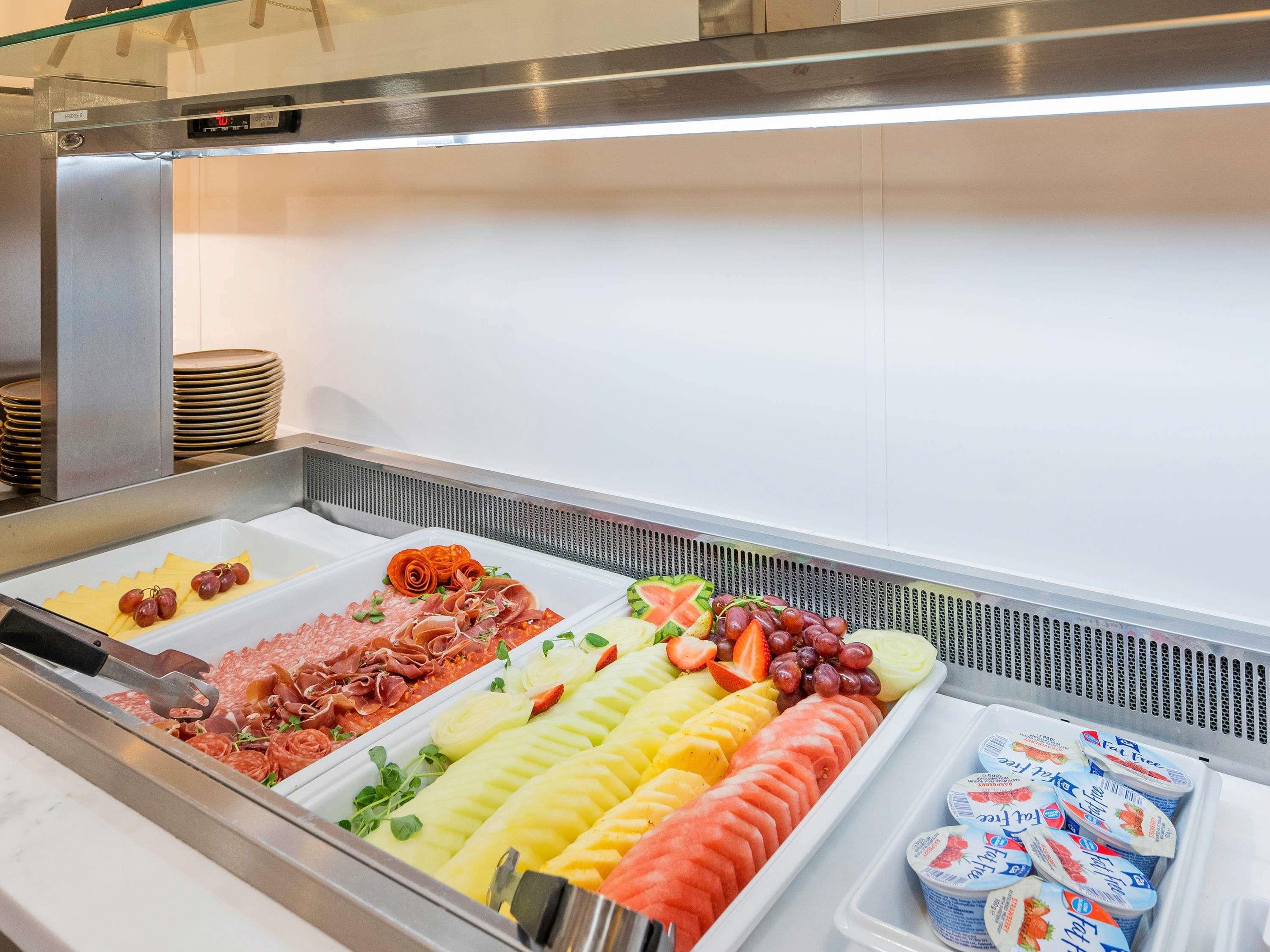 A buffet with various food items including meats, fruits, and yogurt.