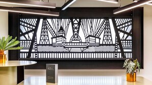 A reception desk with a modern design, featuring a large decorative screen displaying a bridge and buildings. There are two chairs and a potted plant on the desk. - Mercure Newport Hotel (Newport)