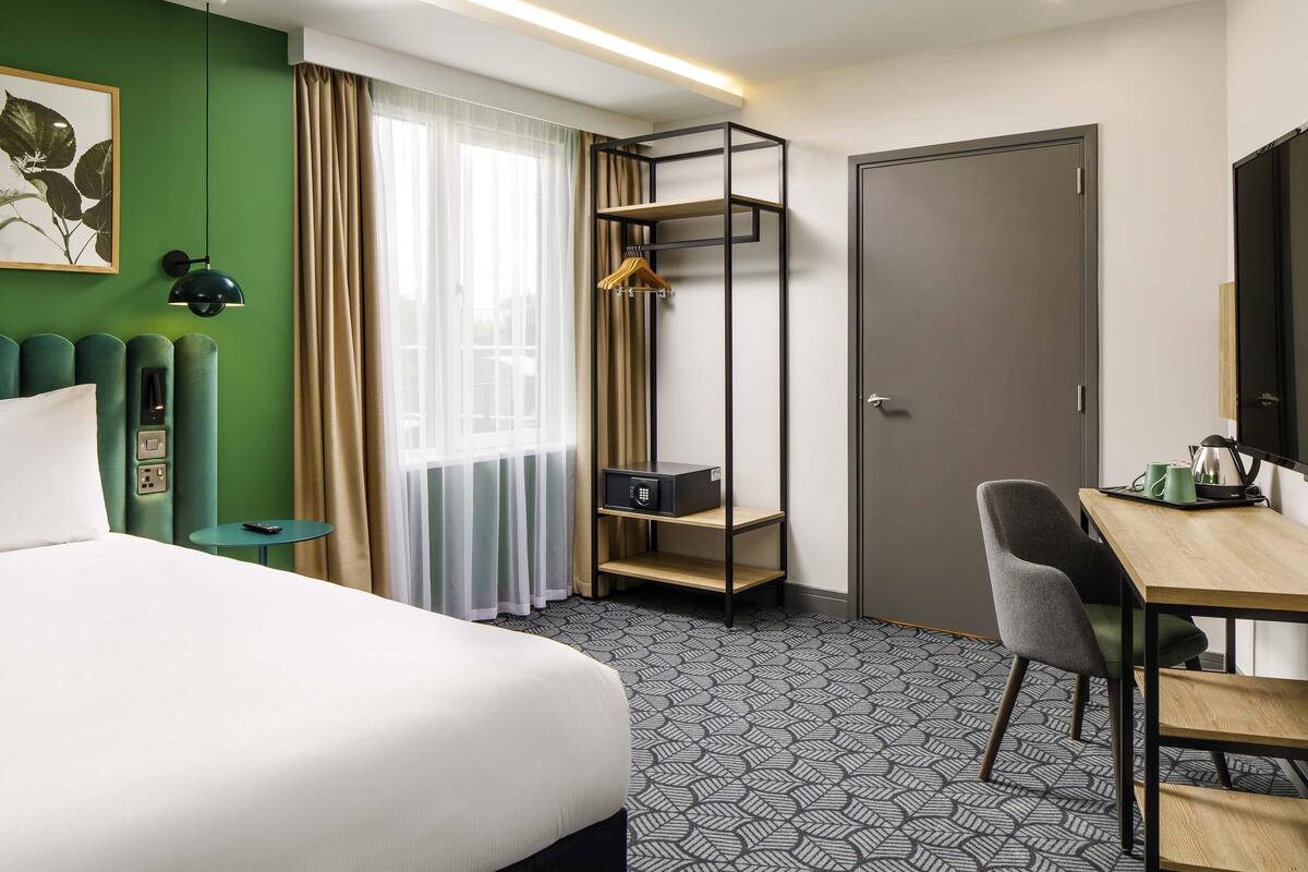 A hotel room with a bed, a desk, a chair, a wardrobe, and a hanging shelf.