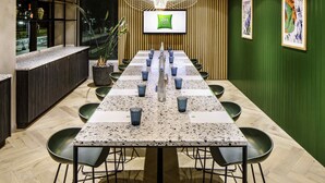 Una sala de conferencias con una larga mesa, sillas, una pantalla de televisión y una planta en maceta.