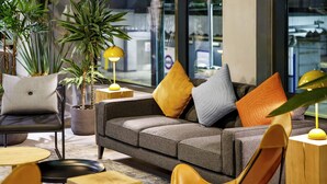 Un interior moderno con un sofá gris, cojines amarillos y anaranjados, mesitas de madera y plantas en macetas.