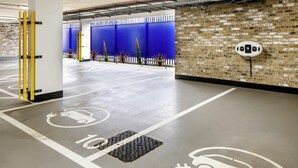 Un garaje de estacionamiento con espacios designados para vehículos eléctricos, un muro de ladrillo y una división azul.