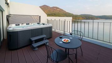 A balcony with a hot tub, a table with chairs, and a view of a lake and mountains.