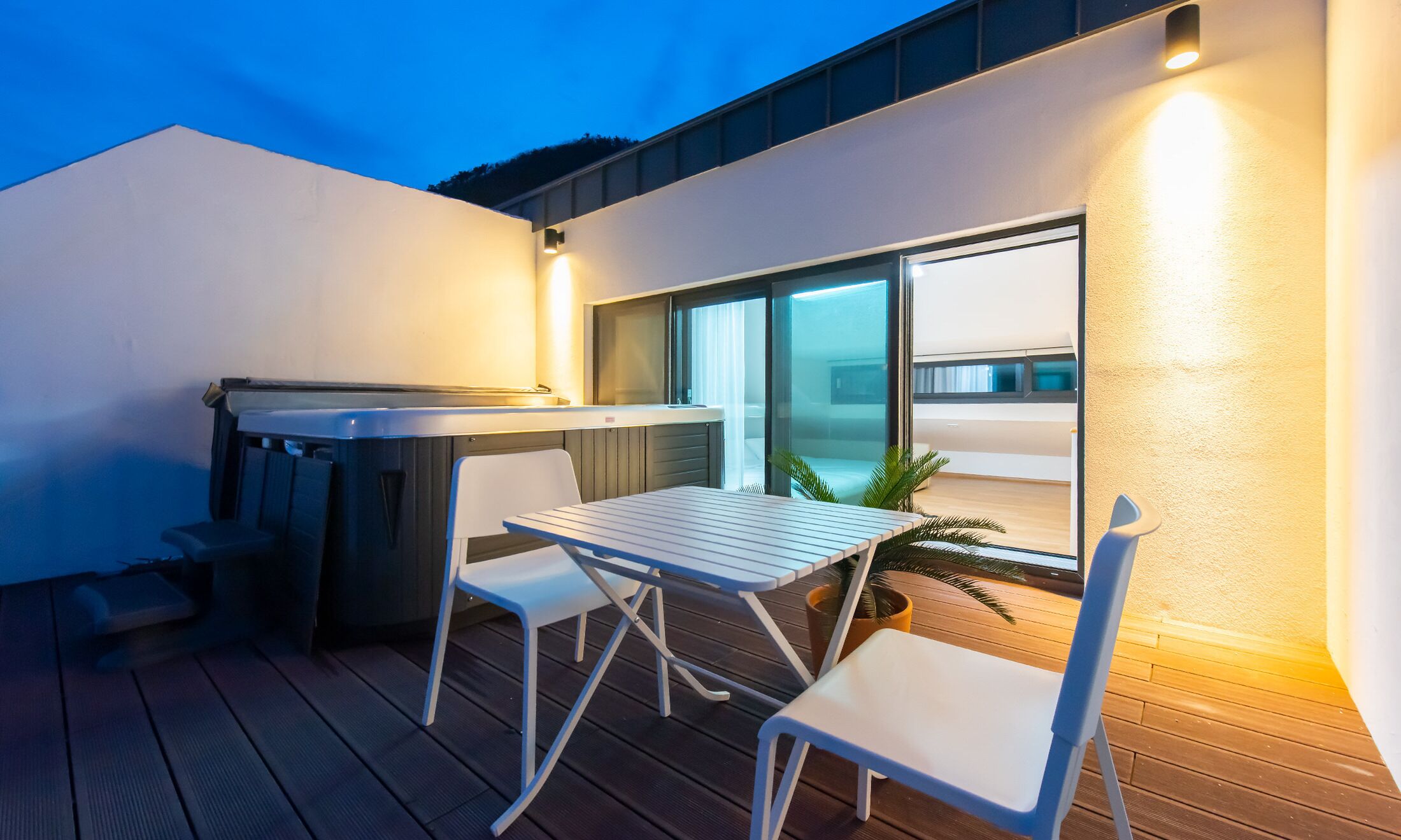 A modern outdoor patio with a hot tub, a table, and two chairs.