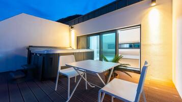 A modern outdoor patio with a hot tub, a table, and two chairs.