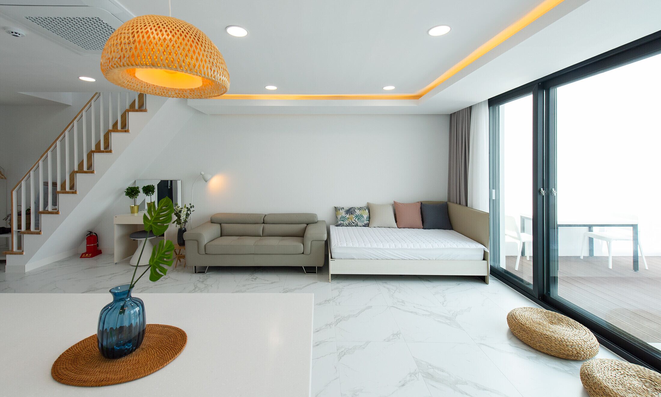 A modern living room with a sofa, a bed, a staircase, and a large window.