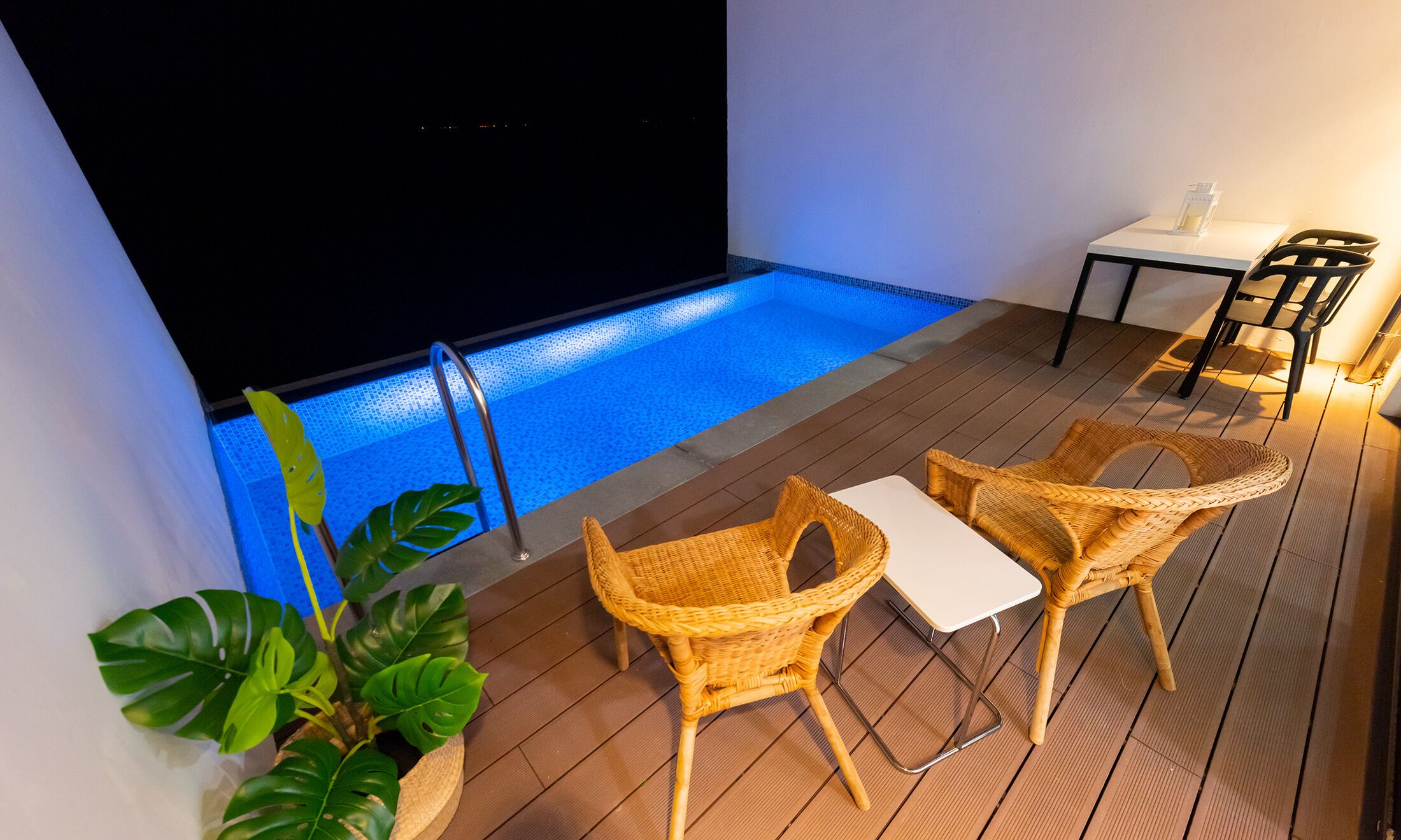 A poolside area with wicker chairs, a small table, and a potted plant.