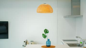 A modern kitchen with a hanging orange woven light fixture, a blue vase with a plant, and a stainless steel sink.