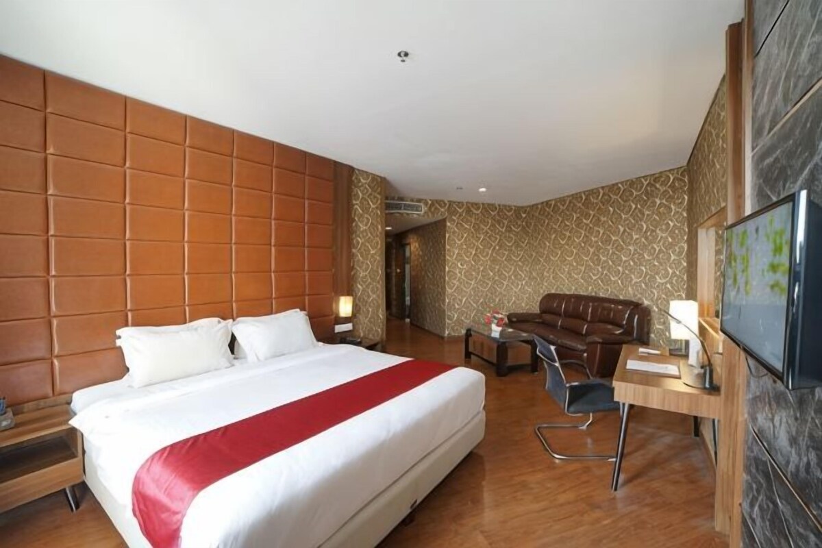 A hotel room with a large bed, a desk, a chair, and a television.