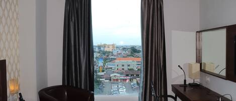 A hotel room with a bed, a desk, a chair, and a large window with curtains.