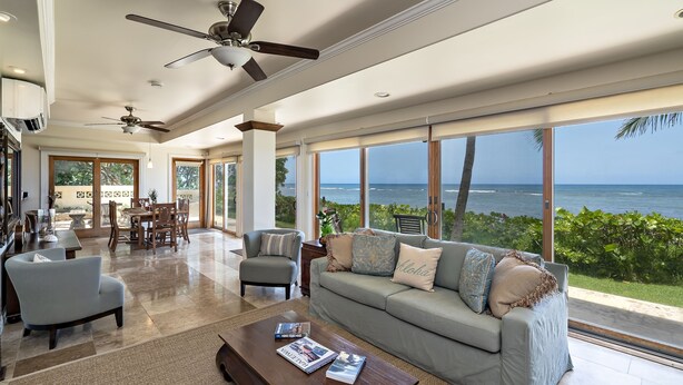 A spacious living room with a large window overlooking the ocean, a ceiling fan, and a cozy seating area.