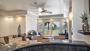 A modern kitchen with a curved granite countertop, a ceiling fan, and a view of the ocean through large windows.