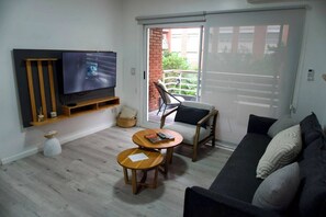 A living room with a flat-screen TV, a sofa, a coffee table, and a chair. There is a sliding glass door leading to an outdoor area. - Puerto Madero - Spectacular apartment (Puerto Madero)