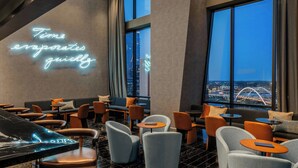 A modern lounge area with seating and tables, a neon sign, and large windows offering a city view. - The Joseph, a Luxury Collection Hotel, Nashville (Nashville)