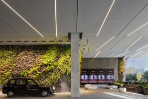 A modern building entrance with a black SUV parked in front, a vertical garden, and a seating area with white benches.