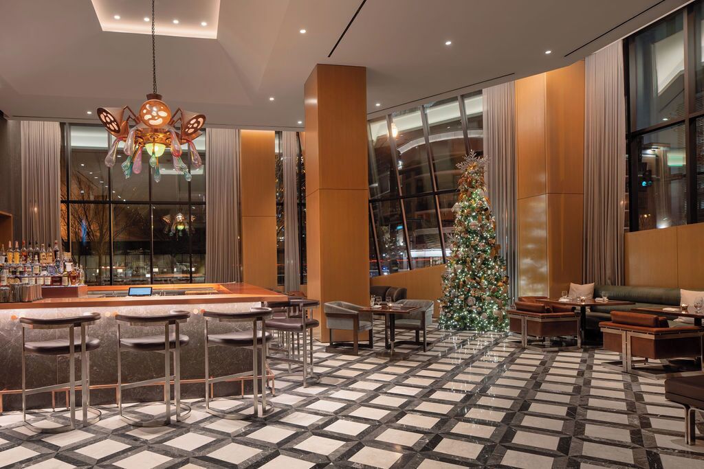 A modern hotel lobby with a bar area, seating, a large Christmas tree, and a checkered floor.